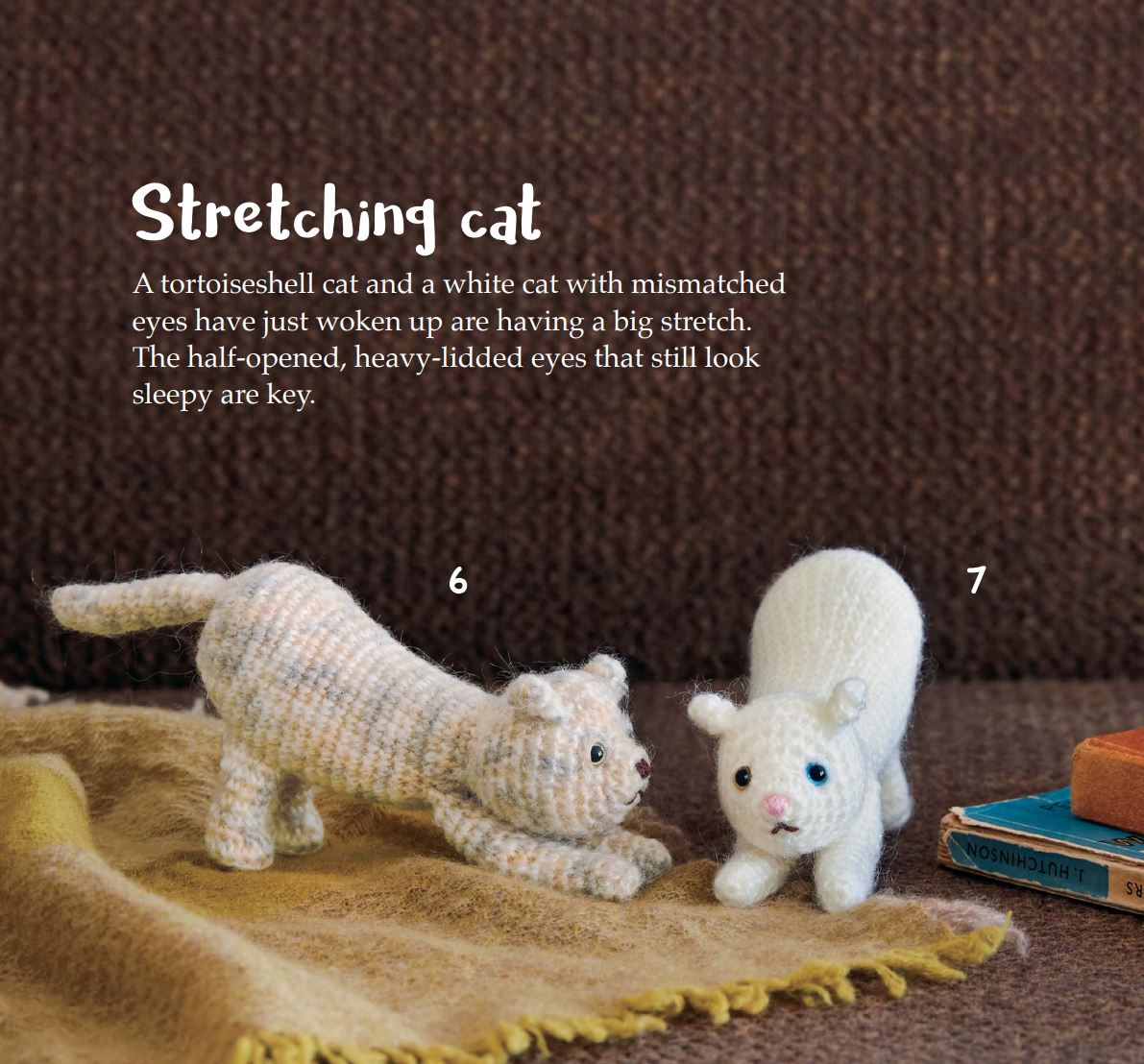 Two amigurumi cats, one beige striped stretching with raised front paws, and one white sitting with blue eyes on a brown.