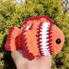 Handheld orange and white striped amigurumi fish with scalloped fins and black eyes.