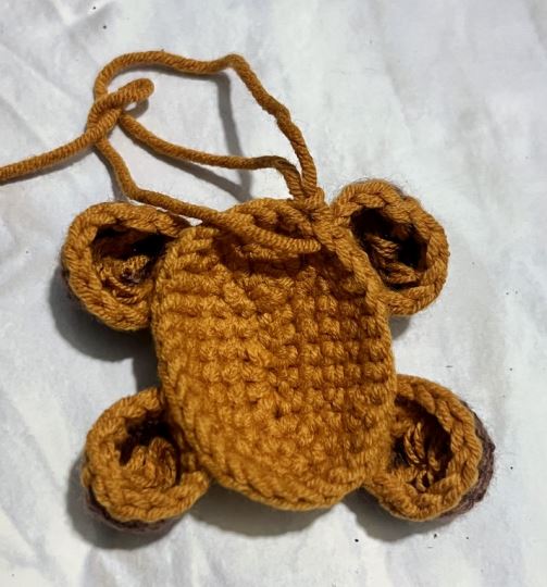Brown crocheted amigurumi Highland cow body with four legs and two ears on white background.