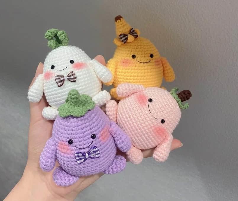Four colorful amigurumi bugs and small critters in pastel shades with embroidered faces and bows, held in hand against a.