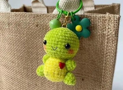 Small green amigurumi chick keychain with a flower and bead charms hanging on a burlap bag handle.