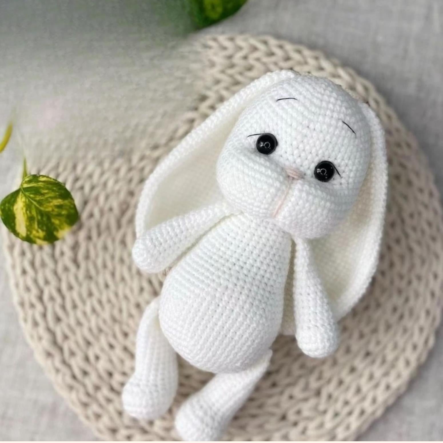 White crocheted amigurumi bunny with black eyes and long ears on a textured beige mat.