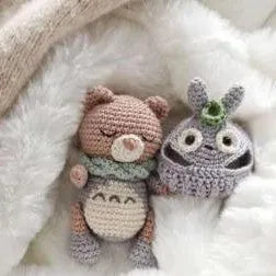 Crochet amigurumi bear with scarf and whimsical gray amigurumi creature with spiral horn on white blanket.