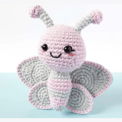 Crochet amigurumi butterfly with pink and gray wings and smiling face.