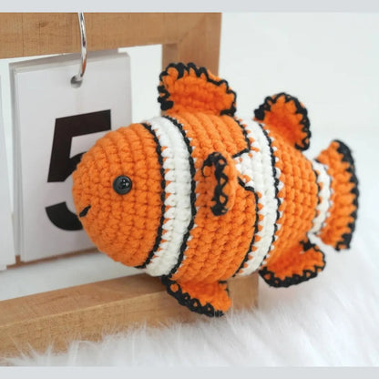 Orange and white striped amigurumi clownfish with black accents next to a wooden calendar block displaying the number 5.