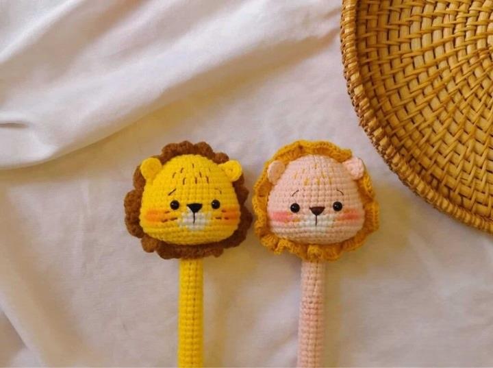 Crocheted amigurumi lion and pink lioness heads with yarn manes on beige fabric background.