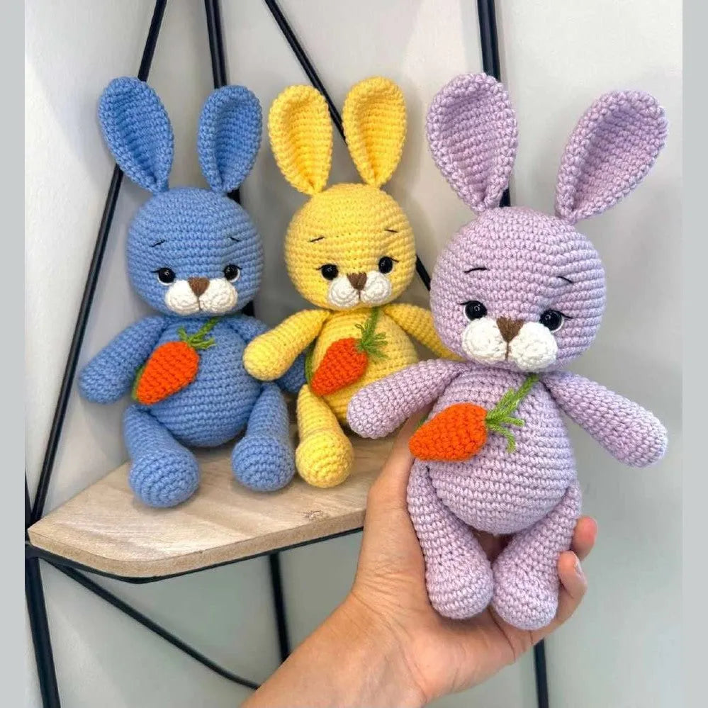 Three colorful amigurumi bunnies in blue, yellow, and lavender holding crocheted carrots.