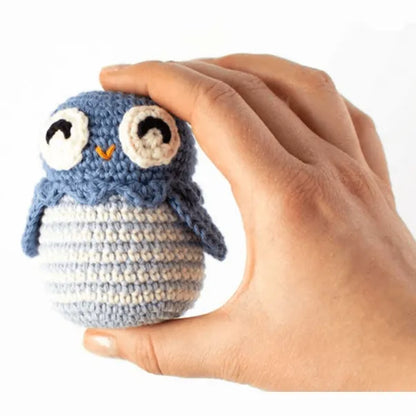 Small blue and white amigurumi owl held between fingers on white background.