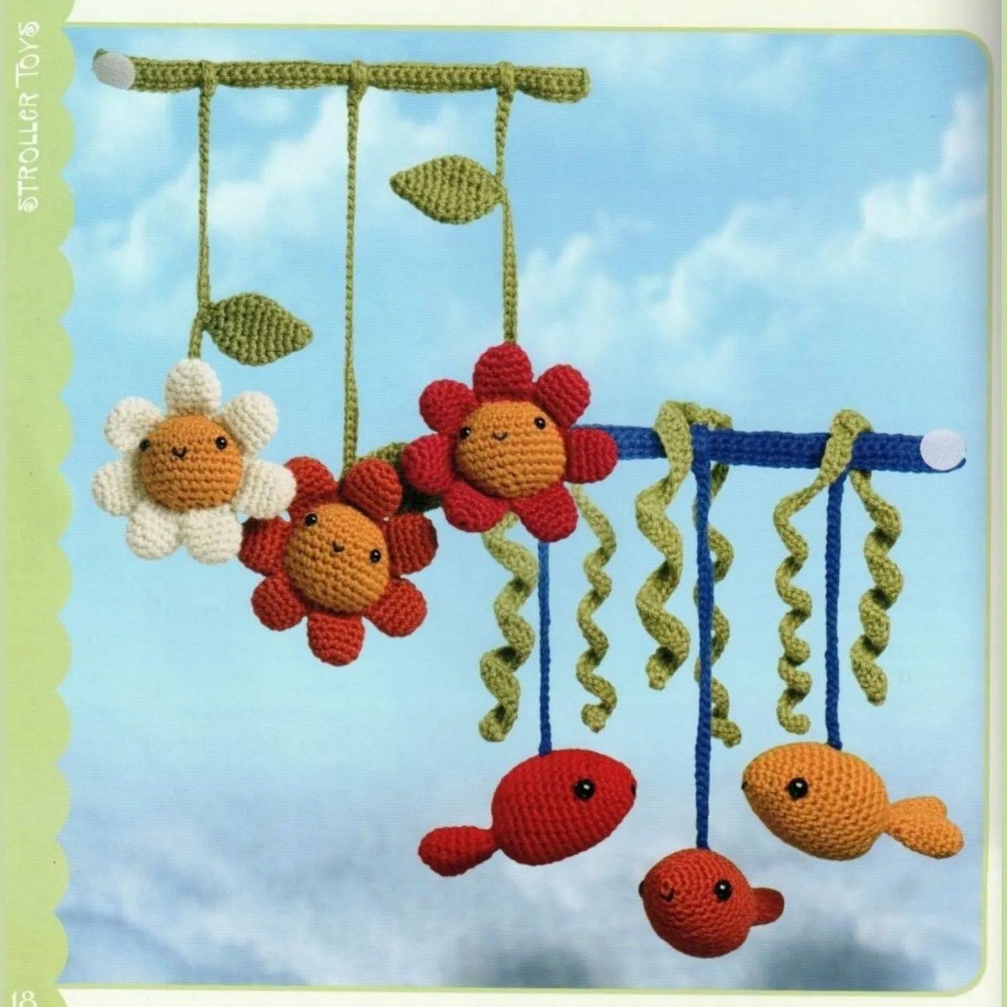 Colorful crocheted amigurumi flowers and fish hanging from rods against a blue sky background.