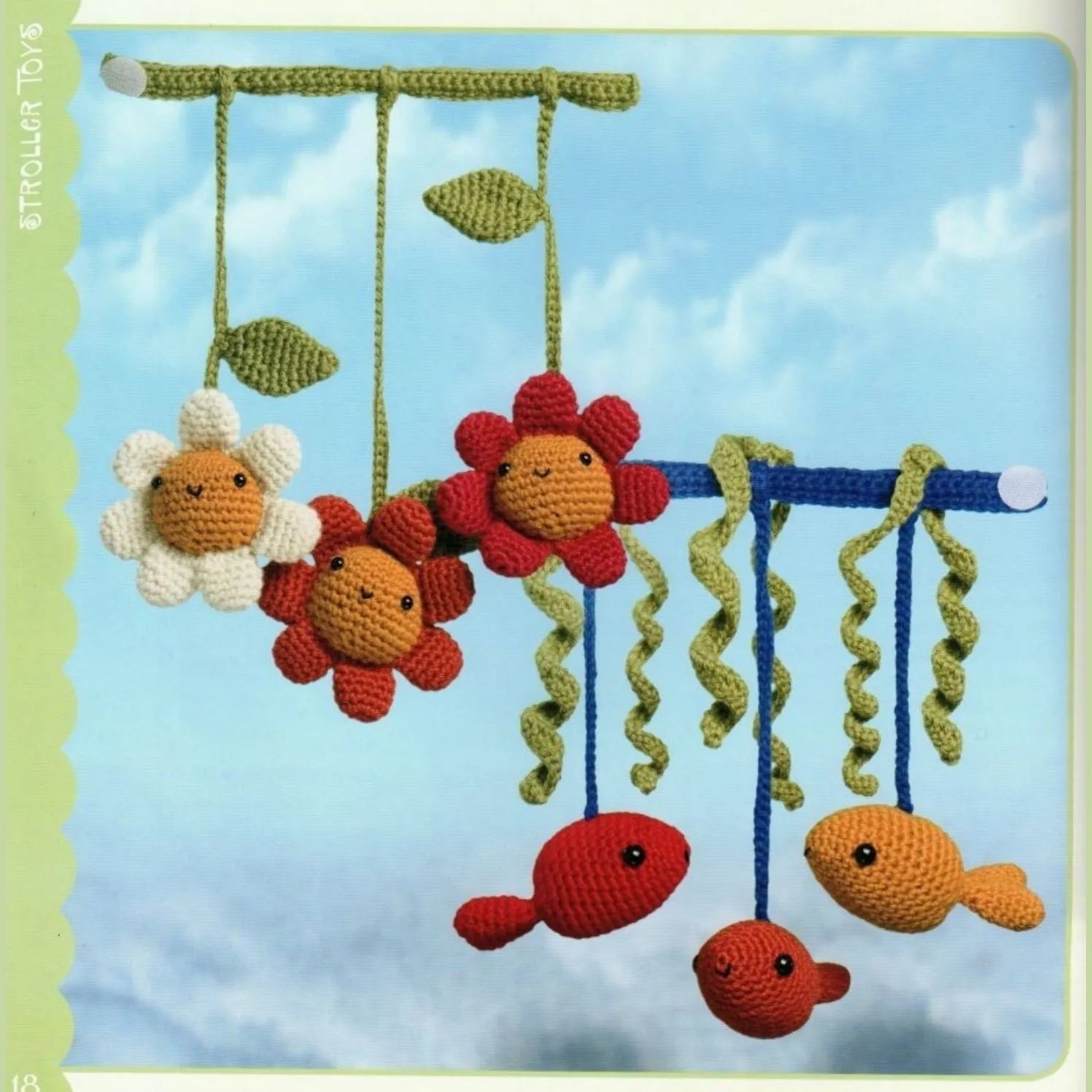 Colorful crocheted amigurumi flowers and fish hanging from rods against a blue sky background.