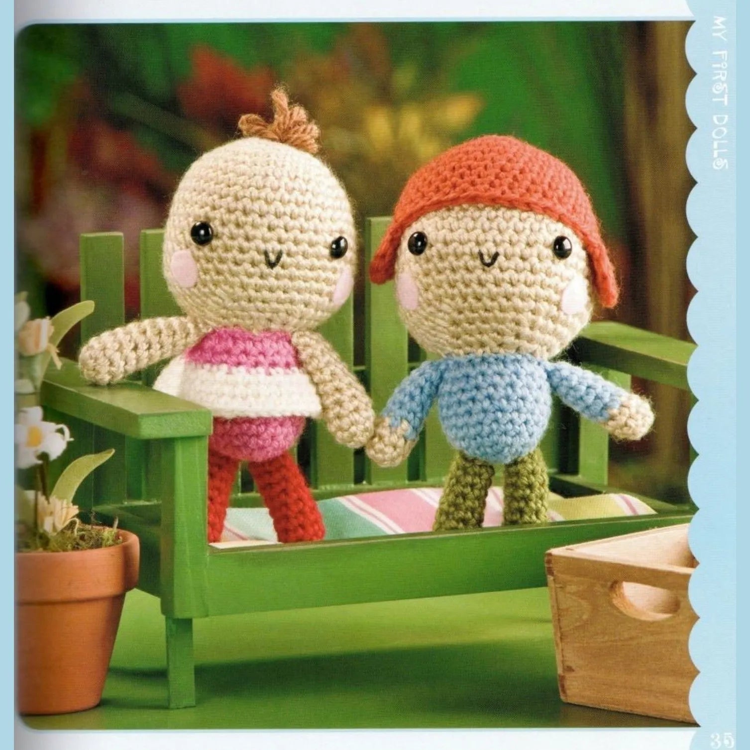 Two colorful amigurumi dolls sitting on a green wooden bench with a blurred garden background.