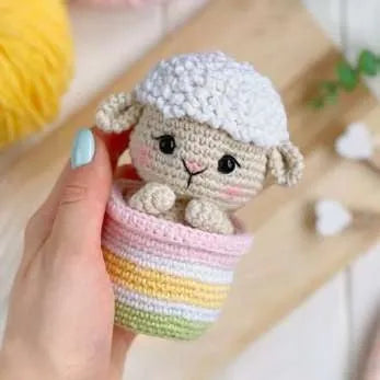 Handcrafted amigurumi lamb with textured wool cap in pastel striped crochet pot.