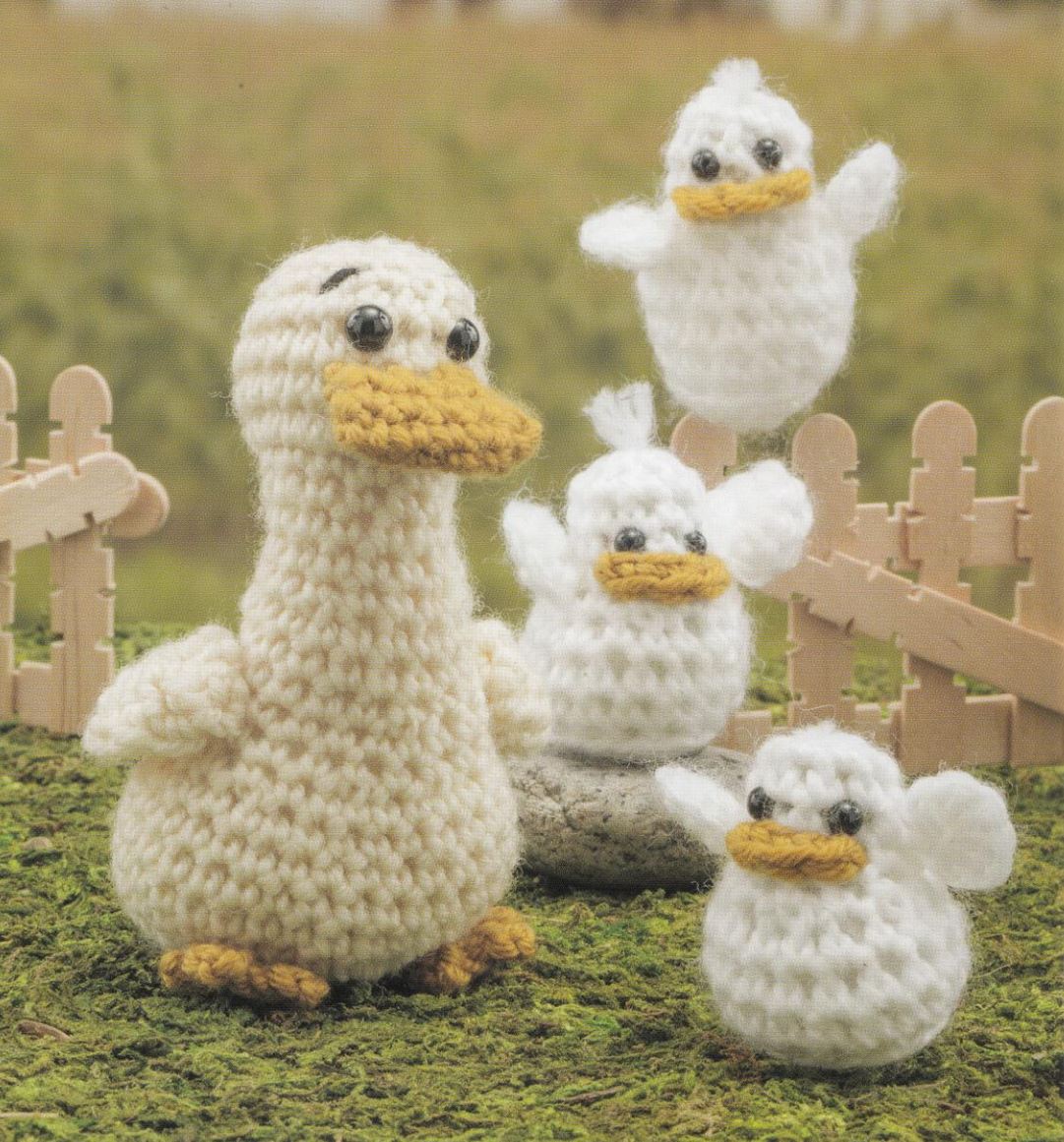 Crocheted amigurumi ducks in cream and yellow with black eyes on grassy background.