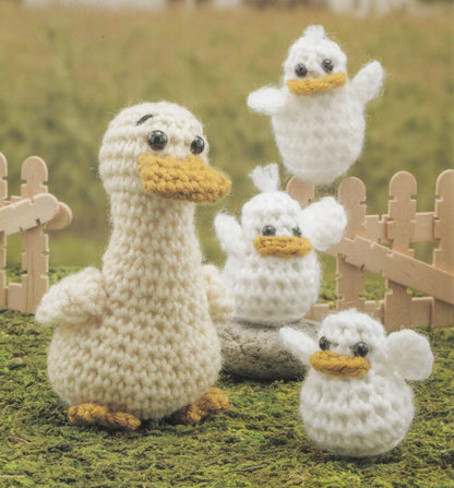 Crocheted amigurumi ducks in cream and yellow with black eyes on grassy background.