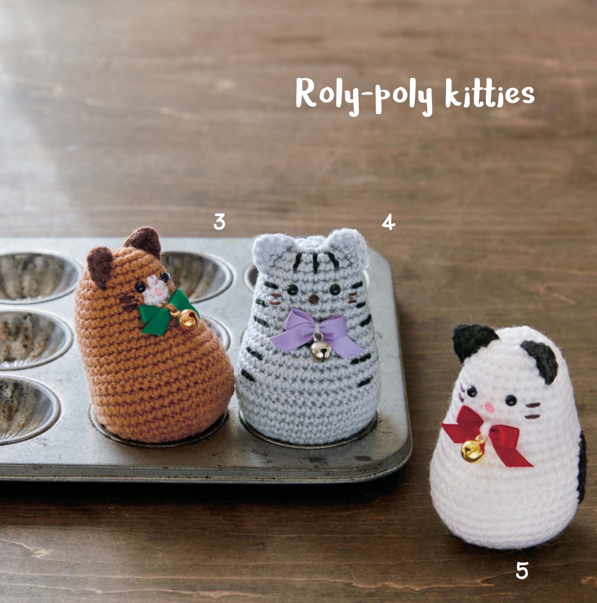 Three crochet amigurumi cats in brown, gray, and white styles with scarves, displayed on a metal tray.