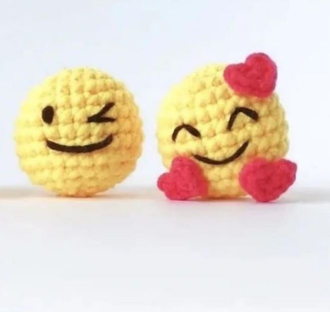 Yellow crochet amigurumi emojis with winking and smiling faces, adorned with small red hearts.