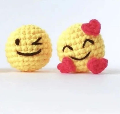 Yellow crochet amigurumi emojis with winking and smiling faces, adorned with small red hearts.