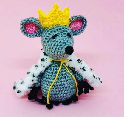 Crochet Mouse King amigurumi with yellow crown and royal fur cape against pink background.