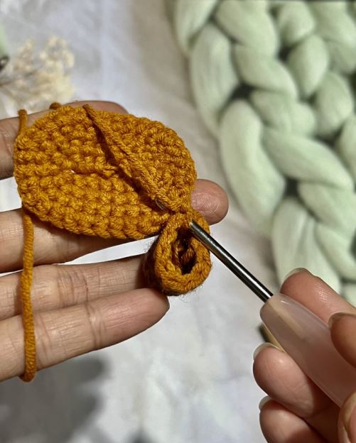 Hand holding crochet hook creating mustard yellow amigurumi piece with chunky cream yarn background.