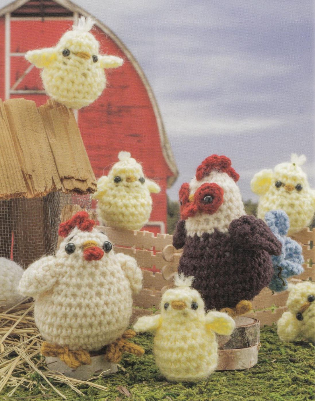 Crochet amigurumi farm animals including chickens and chicks arranged on hay with a red barn backdrop.