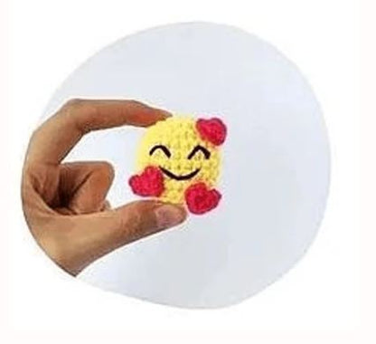 Hand holding small yellow crochet amigurumi emoji with smiling face and red hearts.