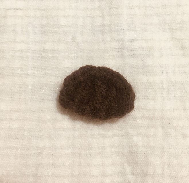 Small dark brown crocheted amigurumi deer nose or head piece on light textured fabric background.