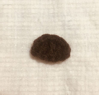 Small dark brown crocheted amigurumi deer nose or head piece on light textured fabric background.
