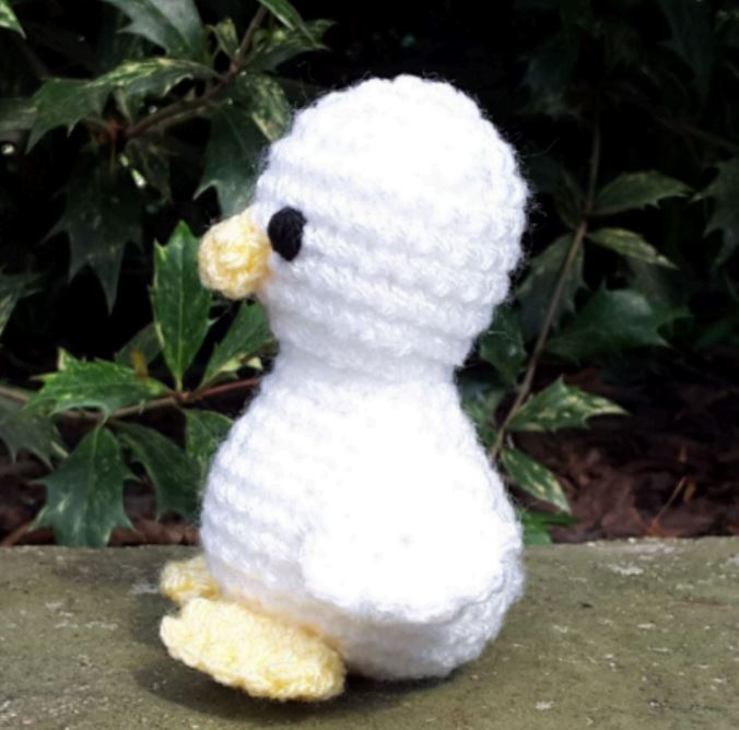White and yellow baby duck amigurumi with black eyes, crocheted texture, standing outdoors.