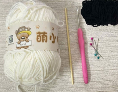 White and black yarn balls with wooden crochet hooks, pink handle, and pins for amigurumi crochet projects.