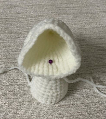 White crocheted amigurumi hood piece on beige fabric background with purple pin.